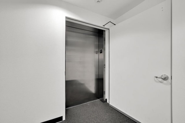 hallway with elevator and dark carpet