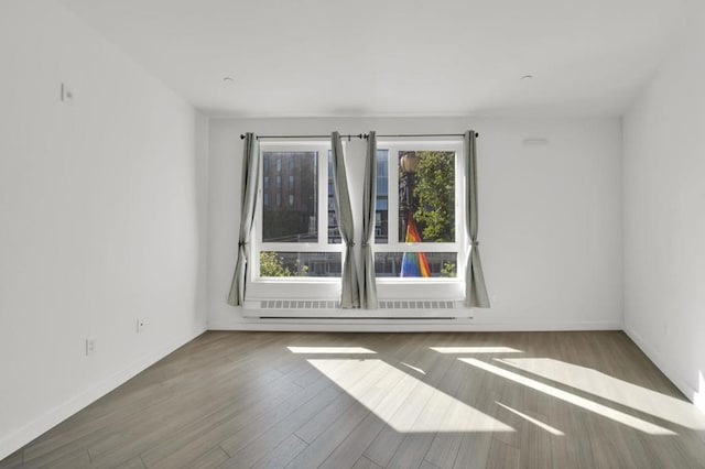 unfurnished room featuring hardwood / wood-style floors, a healthy amount of sunlight, and a baseboard radiator