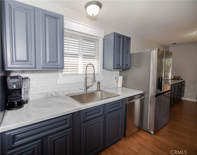 kitchen featuring sink, tasteful backsplash, blue cabinetry, appliances with stainless steel finishes, and hardwood / wood-style floors