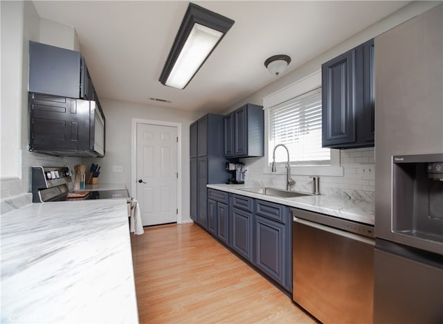 kitchen with blue cabinetry, stainless steel appliances, light wood-type flooring, and decorative backsplash