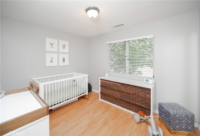 bedroom featuring light wood-type flooring and a nursery area