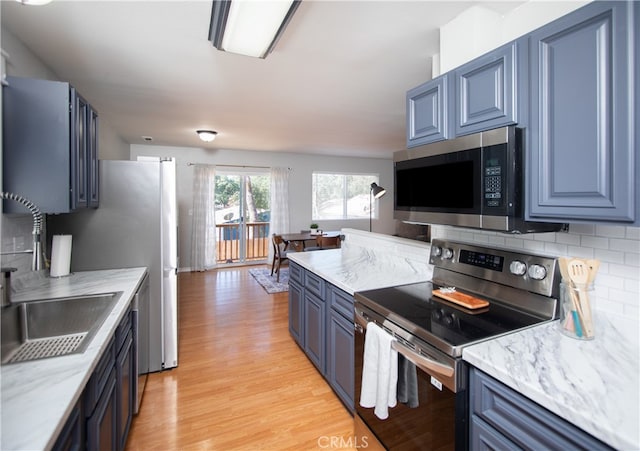 kitchen with appliances with stainless steel finishes, blue cabinets, light wood-type flooring, and tasteful backsplash