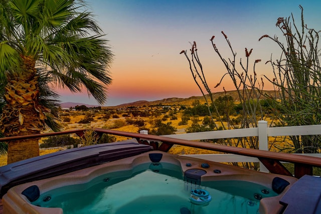 pool at dusk with a hot tub and a mountain view