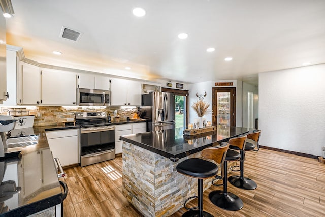 kitchen featuring appliances with stainless steel finishes, decorative backsplash, white cabinetry, a kitchen island, and light hardwood / wood-style flooring