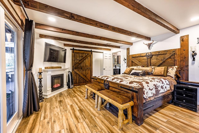 bedroom with beamed ceiling, light wood-type flooring, and a barn door