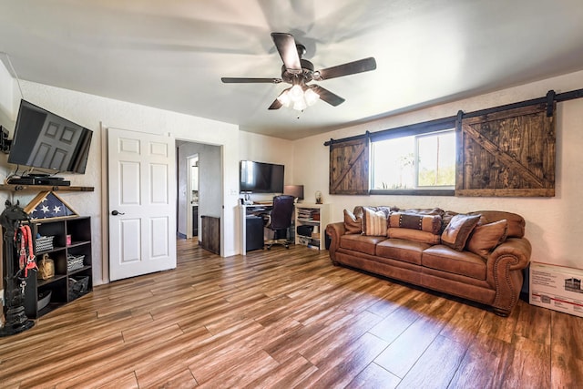 living room with wood-type flooring, ceiling fan, and a barn door