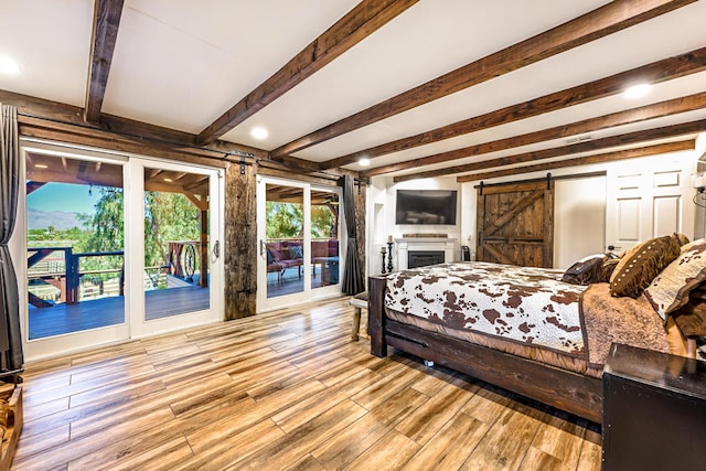 bedroom featuring access to outside, light wood-type flooring, beam ceiling, and a barn door