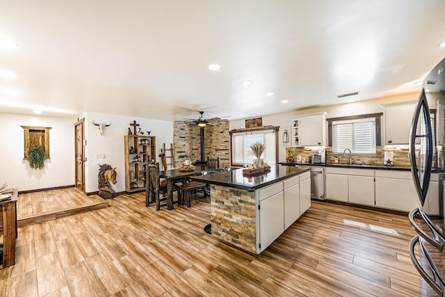 kitchen featuring a wood stove, white cabinetry, stainless steel appliances, a center island, and light wood-type flooring