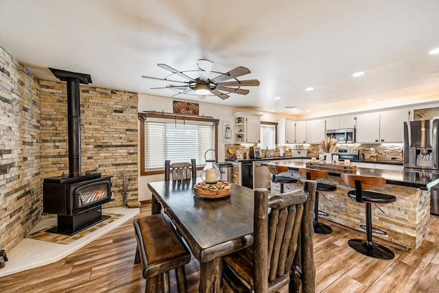 dining room with a wood stove, light hardwood / wood-style floors, and ceiling fan