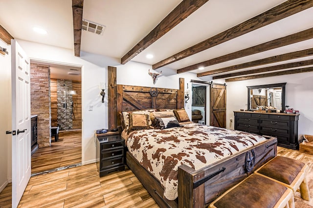 bedroom with light wood-type flooring, a barn door, and beamed ceiling