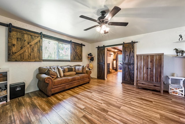 living room with a barn door, ceiling fan, and hardwood / wood-style flooring