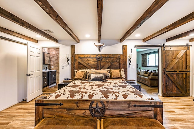 bedroom featuring wine cooler, a barn door, beamed ceiling, light hardwood / wood-style flooring, and ensuite bathroom