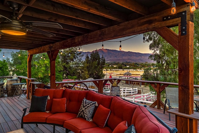 deck at dusk with an outdoor living space, ceiling fan, and a mountain view