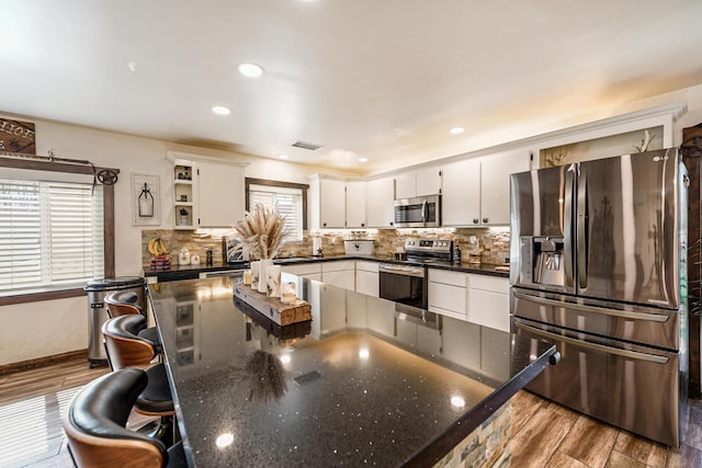 kitchen with a breakfast bar, light hardwood / wood-style floors, white cabinetry, decorative backsplash, and stainless steel appliances