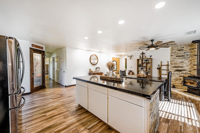 kitchen with ceiling fan, white cabinets, a wood stove, stainless steel refrigerator, and a center island