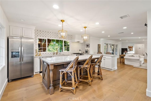 kitchen featuring visible vents, stainless steel refrigerator with ice dispenser, white cabinetry, tasteful backsplash, and a sink