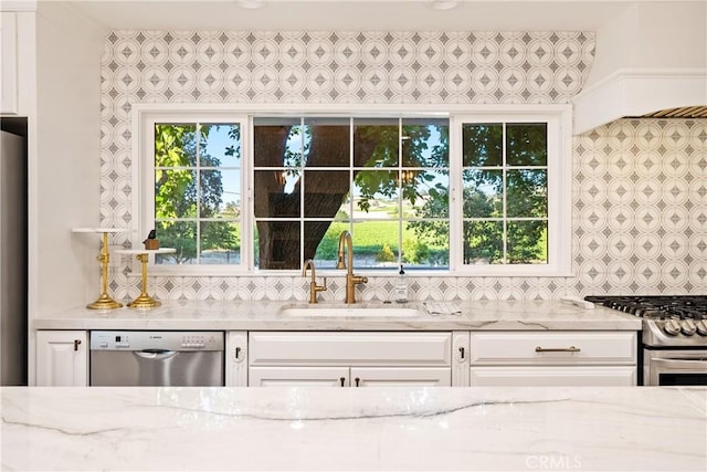 interior space featuring white cabinets, appliances with stainless steel finishes, a sink, and light stone counters