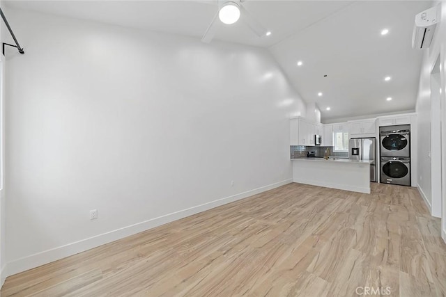 unfurnished living room featuring a wall mounted air conditioner, light hardwood / wood-style flooring, vaulted ceiling, ceiling fan, and stacked washer / dryer