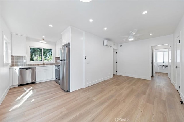 kitchen with an AC wall unit, ceiling fan, white cabinets, and stainless steel appliances