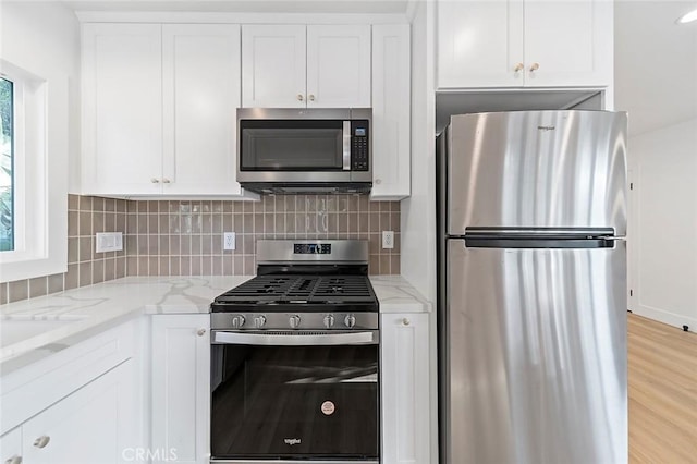 kitchen featuring light stone countertops, tasteful backsplash, stainless steel appliances, white cabinets, and light hardwood / wood-style floors