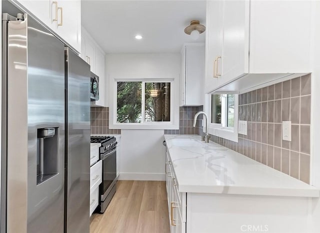 kitchen featuring white cabinets, sink, light hardwood / wood-style floors, light stone counters, and stainless steel appliances