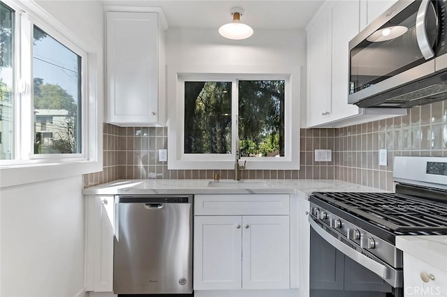 kitchen featuring tasteful backsplash, light stone counters, stainless steel appliances, sink, and white cabinetry