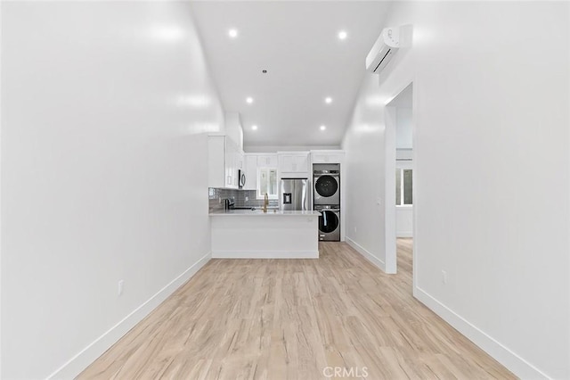 unfurnished living room featuring light wood-type flooring, an AC wall unit, and stacked washer and clothes dryer