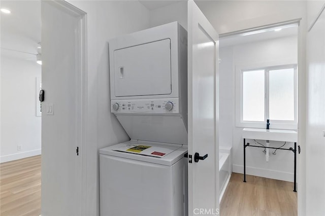 washroom with sink, light hardwood / wood-style floors, and stacked washer and clothes dryer