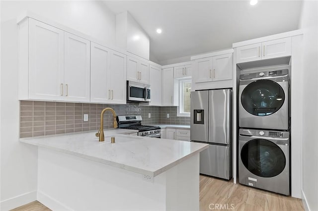 kitchen with kitchen peninsula, stainless steel appliances, white cabinets, and stacked washer / drying machine