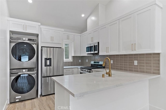 kitchen featuring light stone countertops, stacked washing maching and dryer, kitchen peninsula, white cabinets, and appliances with stainless steel finishes