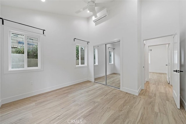 unfurnished bedroom featuring ceiling fan, a towering ceiling, light hardwood / wood-style floors, a wall unit AC, and a closet