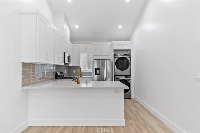 kitchen with sink, stainless steel appliances, lofted ceiling, white cabinets, and stacked washer and clothes dryer