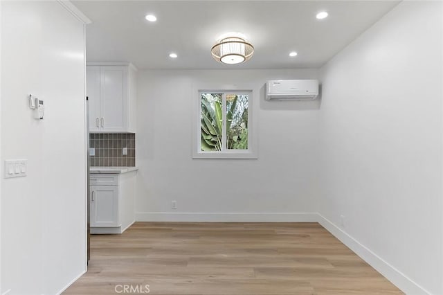 unfurnished dining area featuring a wall mounted AC and light hardwood / wood-style floors