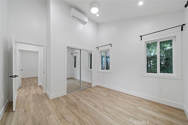 unfurnished bedroom with an AC wall unit, a closet, a towering ceiling, and light wood-type flooring