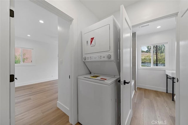 clothes washing area featuring light wood-type flooring and stacked washer and dryer