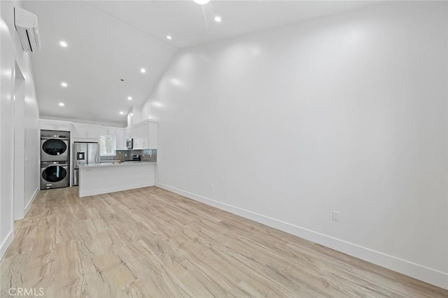 unfurnished living room featuring a wall unit AC, high vaulted ceiling, stacked washing maching and dryer, and light wood-type flooring