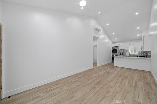 unfurnished living room with stacked washer and dryer, vaulted ceiling, ceiling fan, light hardwood / wood-style floors, and a wall unit AC