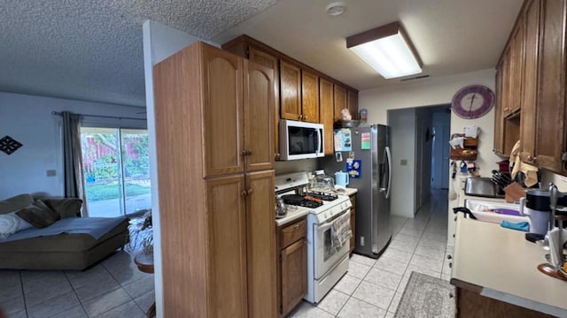 kitchen featuring a textured ceiling, light tile patterned floors, white gas range oven, and stainless steel refrigerator