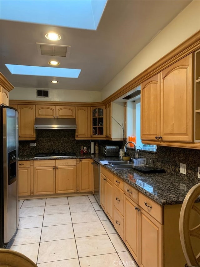 kitchen featuring dark stone countertops, light tile patterned floors, a skylight, and stainless steel appliances