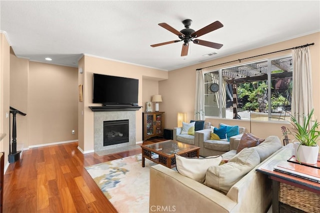 living room with a fireplace, ceiling fan, light hardwood / wood-style flooring, and ornamental molding