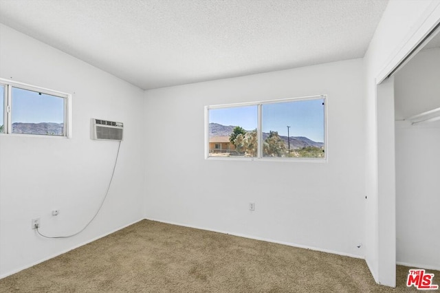 unfurnished bedroom featuring a wall mounted air conditioner, a textured ceiling, carpet floors, and a closet