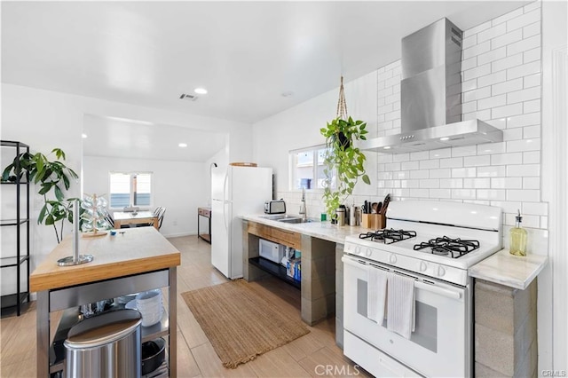 kitchen with white appliances, wall chimney exhaust hood, decorative backsplash, sink, and light wood-type flooring