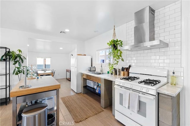 kitchen featuring white appliances, visible vents, wall chimney exhaust hood, light countertops, and backsplash