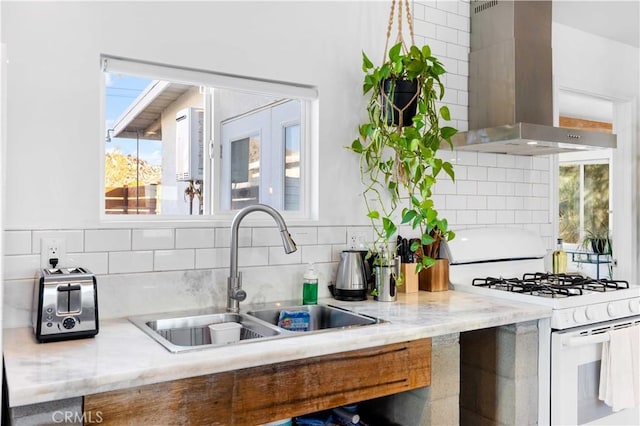 kitchen featuring tasteful backsplash, white gas range oven, light stone countertops, wall chimney range hood, and a sink