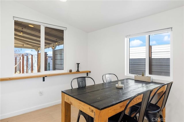 dining room with light wood-style floors, vaulted ceiling, and baseboards