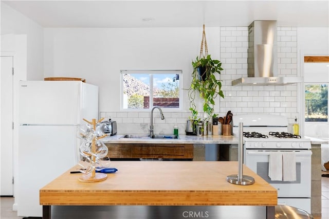 kitchen with wall chimney exhaust hood, white appliances, a sink, and decorative backsplash