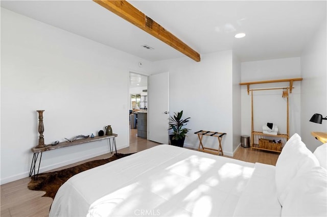 bedroom featuring baseboards, visible vents, beamed ceiling, and wood finished floors