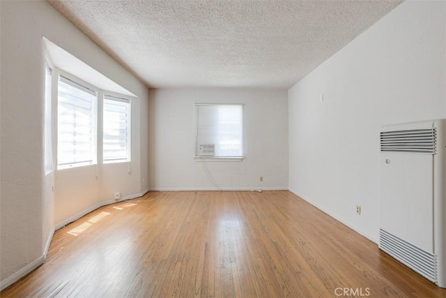 spare room with heating unit, a textured ceiling, and light hardwood / wood-style flooring