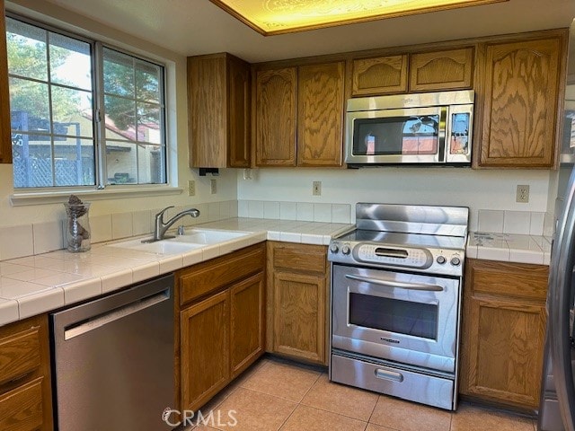 kitchen with light tile patterned flooring, stainless steel appliances, sink, and tile countertops