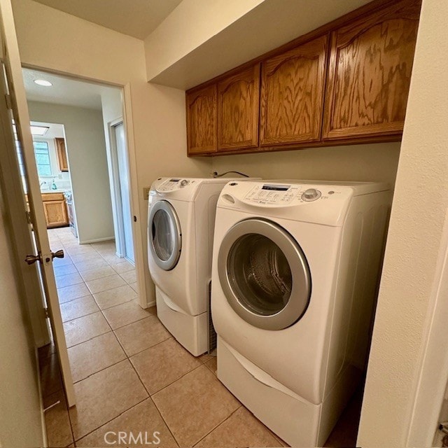 laundry room with washing machine and clothes dryer, cabinets, and light tile patterned floors